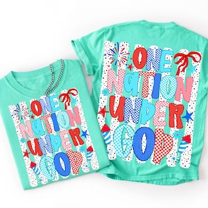 Puede incluir: Dos camisetas verde menta con el texto "ONE NATION UNDER GOD" en letras de burbujas rojas, azules y rosas. El dise&ntilde;o incluye fuegos artificiales, estrellas y un lazo. Las camisetas son probablemente para un d&iacute;a festivo patri&oacute;tico.