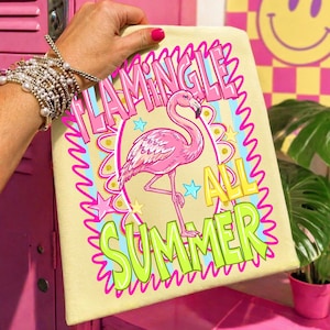 Puede incluir: Una toalla de color amarillo claro con una ilustraci&oacute;n de flamenco rosa y las palabras "Flamingle All Summer" en rosa y verde. El flamenco est&aacute; de pie sobre una pierna, rodeado de estrellas.