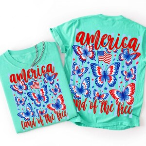 May include: A mint green t-shirt featuring a graphic print of red, white, and blue butterflies, an American flag, and the red text "america" and "land of the free". The design includes light blue vertical stripes and small star accents.