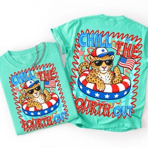Op de afbeelding: Twee turquoise t-shirts met een afbeelding van een luipaard met een zonnebril en een patriottische hoed, drijvend in een rood, wit en blauw zwemband, met een Amerikaanse vlag. De tekst luidt "Chill the Fourth Out."