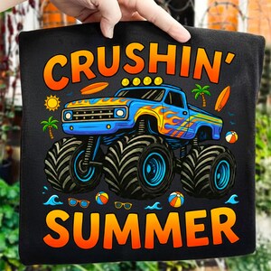May include: Black t-shirt with a colorful graphic of a monster truck with flames, palm trees, and the words "CRUSHIN' SUMMER". The truck is blue with yellow and orange flames. Includes images of a sun, surfboards, and beach balls.