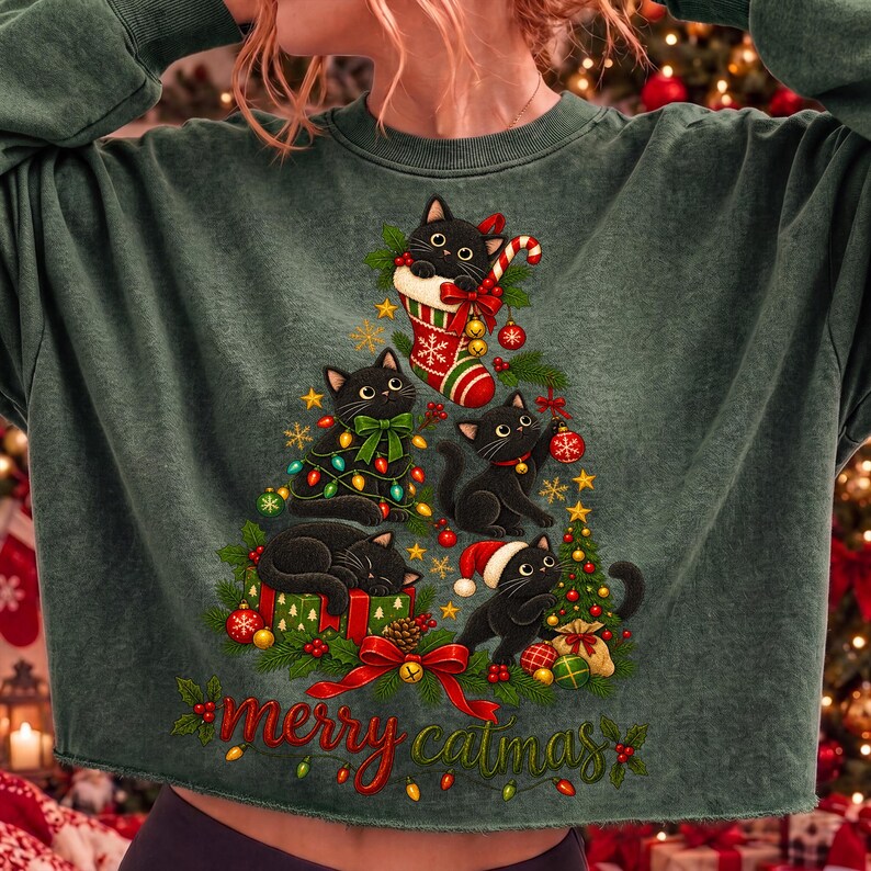 K&ouml;nnte beinhalten: Ein dunkelgr&uuml;nes Langarm-Sweatshirt mit einer Grafik von vier schwarzen Katzen in Form eines Weihnachtsbaums. Das Design zeigt einen rot-wei&szlig;en Strumpf, ein rotes Geschenk, Christbaumkugeln, Tannenzweige und den roten Schriftzug merry catmas.
