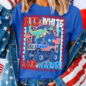 May include: Blue t-shirt with a patriotic graphic. The design features a green dinosaur wearing sunglasses, atop a monster truck with an American flag. The text reads "RED WHITE AND RAWR!"