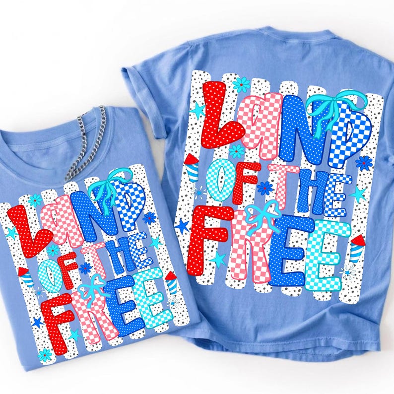 Puede incluir: Una camiseta azul claro con un estampado gr&aacute;fico que dice LAND OF THE FREE en patrones de cuadros y lunares rojos, blancos y azules. El dise&ntilde;o incluye peque&ntilde;os lazos azules, estrellas y fuegos artificiales sobre un fondo de puntos negros.