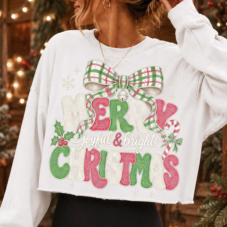 K&ouml;nnte beinhalten: Ein wei&szlig;es, lang&auml;rmeliges, bauchfreies Sweatshirt mit einem Grafikdruck einer gro&szlig;en gr&uuml;n-roten karierten Schleife &uuml;ber dem Text Merry Christmas in einer stilisierten Schriftart, erg&auml;nzt durch den Schriftzug joyful & bright.