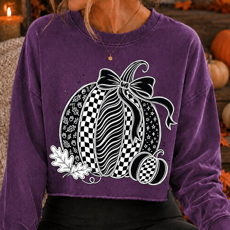 K&ouml;nnte beinhalten: Ein violettes Langarm-Sweatshirt mit einer gro&szlig;en Grafik von zwei K&uuml;rbissen. Der Hauptk&uuml;rbis hat ein schwarz-wei&szlig;es Karomuster, Wellenlinien und eine Schleife. Das Design enth&auml;lt wei&szlig;e Eichenbl&auml;tter, Eicheln und Sterne als grafische Elemente.