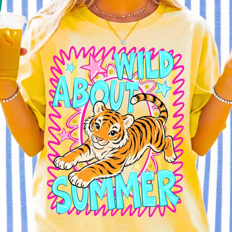 K&ouml;nnte beinhalten: Gelbes T-Shirt mit einem Tiger-Grafik und dem Text "WILD ABOUT SUMMER" in T&uuml;rkis und Pink. Der Tiger ist orange und schwarz, umgeben von Sternen und einem wellenf&ouml;rmigen rosa Rahmen.