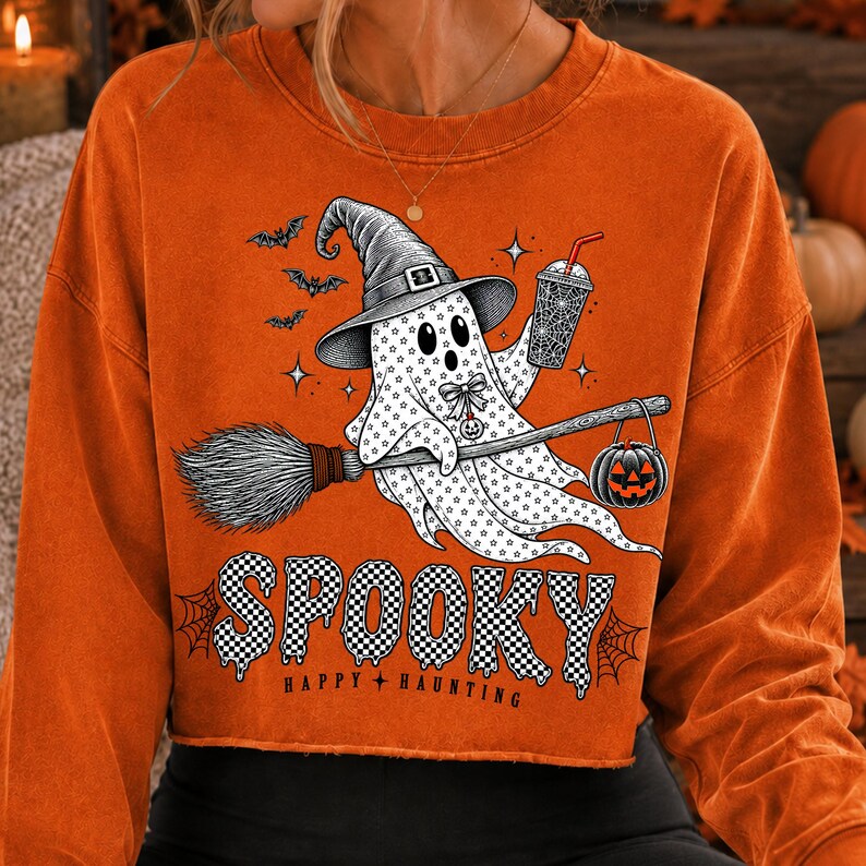 May include: An orange long-sleeve sweatshirt featuring a graphic of a ghost wearing a witch hat, holding a drink, and riding a broomstick with a jack-o'-lantern. The design includes bats, stars, and the text "SPOOKY HAPPY HAUNTING" in a checkered font.