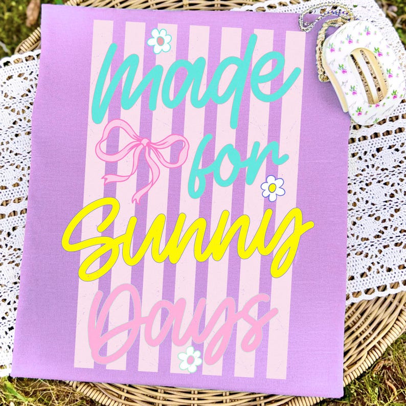 K&ouml;nnte beinhalten: Eine lavendelfarbene Tragetasche mit vertikalen rosa und wei&szlig;en Streifen und den Worten "Made for Sunny Days" in T&uuml;rkis, Rosa und Gelb. Eine kleine, blumenmusternde Handtasche mit goldener Kette ist oben rechts zu sehen.