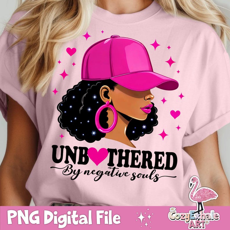 May include: Pink graphic tee with a black and white illustration of a woman wearing a pink baseball cap and large hoop earrings. The text "Unbothered by negative souls" is printed on the shirt.