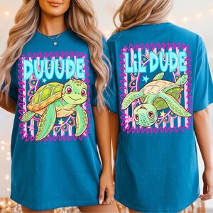 May include: Teal t-shirt with a cartoon turtle design. The front says "DUUUDE" and the back says "Lil DUDE". The turtle is green and yellow, with pink accents. The design is framed by a pink and white wavy border.