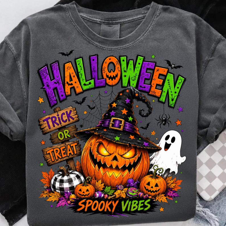 May include: A charcoal grey t-shirt featuring a colourful Halloween graphic. The design includes a large jack-o'-lantern wearing a witch hat, a white ghost, a black and white buffalo plaid pumpkin, and a wooden sign reading Trick or Treat.