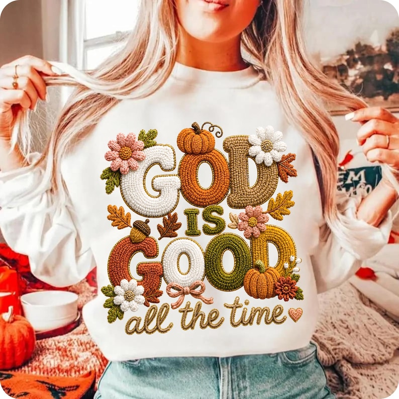 Pu&ograve; includere: Una felpa bianca a maniche lunghe con un design grafico che riporta il testo "GOD IS GOOD all the time" in uno stile ricamato e testurizzato. Il design include elementi autunnali colorati come zucche, ghiande e vari tipi di fiori.