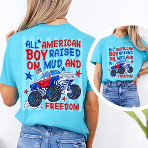 K&ouml;nnte beinhalten: Hellblaues T-Shirt mit einem Monster-Truck-Motiv und dem Text "ALL AMERICAN BOY RAISED ON MUD AND FREEDOM" in Rot, Wei&szlig; und Blau. Das Design enth&auml;lt Sterne und eine amerikanische Flagge.