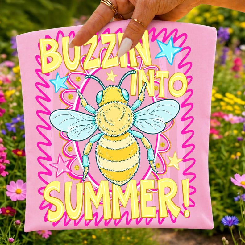 K&ouml;nnte beinhalten: Rosafarbenes Grafik-T-Shirt mit einer Cartoon-Bienen-Illustration. Das T-Shirt tr&auml;gt den Text "BUZZIN' INTO SUMMER!" in gelben Blockbuchstaben. Die Biene ist gelb und blau, mit einem rosa-gelben Hintergrund.