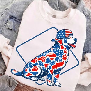 May include: White sweatshirt featuring a patriotic dog design. The dog is wearing a baseball cap with an American flag pattern and has a body covered in red, white, and blue stars, paw prints, and stripes. The design is inside a blue diamond.