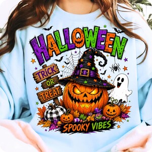 May include: A light blue sweatshirt featuring a colourful Halloween graphic. The design includes a large jack-o'-lantern wearing a witch hat, a white ghost, a buffalo plaid pumpkin, autumn leaves, bats, and the text "HALLOWEEN TRICK OR TREAT SPOOKY VIBES."