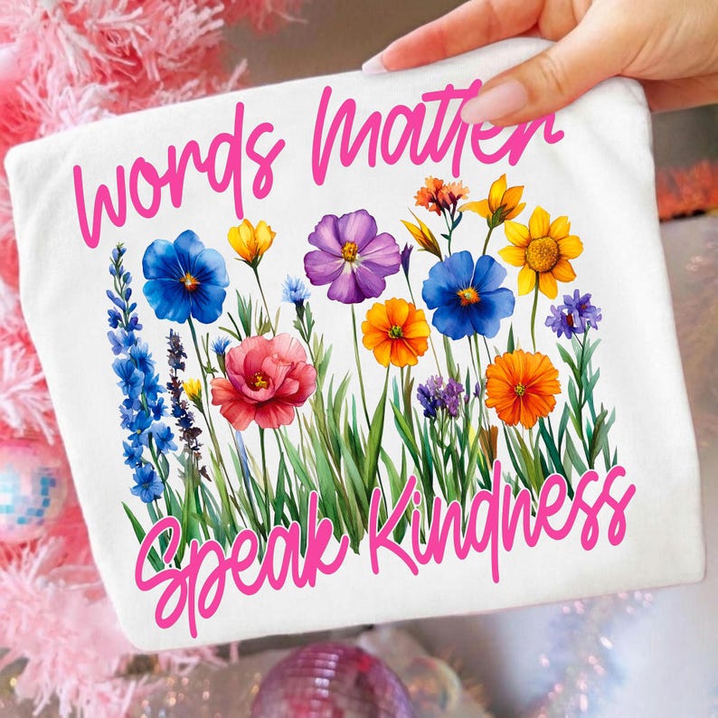 Mockup of 'Words Matter Speak Kindness' design on a white t-shirt, surrounded by wildflowers.