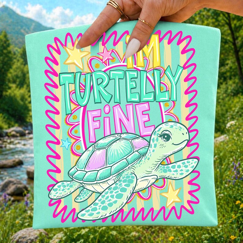 May include: A light teal tote bag with a cartoon turtle illustration and the text "I'm Turtelly Fine". The turtle has a teal shell with pink accents and is surrounded by stars and a pink zig-zag border.