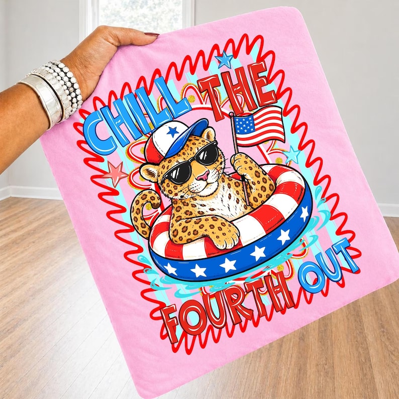 Op de afbeelding: Roze deken met een cartoonluipaard met een zonnebril en een patriotische hoed, drijvend in een rood, wit en blauw zwemband. De deken heeft de tekst "Chill the Fourth Out" met een Amerikaanse vlag.