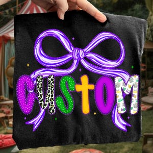 May include: Black fabric with a purple bow and the word "CUSTOM" in various colors and patterns. The letters are purple polka dots, leopard print, green polka dots, yellow, purple, and a white and purple pattern.