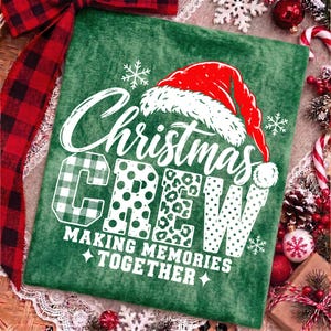 May include: A green fabric item featuring a white graphic that reads Christmas CREW MAKING MEMORIES TOGETHER. The text is topped with a red and white Santa hat and accented with white snowflakes. The letters feature plaid, polka dot, and leopard patterns.
