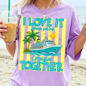 May include: A light purple t-shirt with a graphic of a cruise ship, palm trees, and a sun. The text reads "I LOVE IT when we're Cruisin TOGETHER" in turquoise and yellow. The shirt is a relaxed fit.