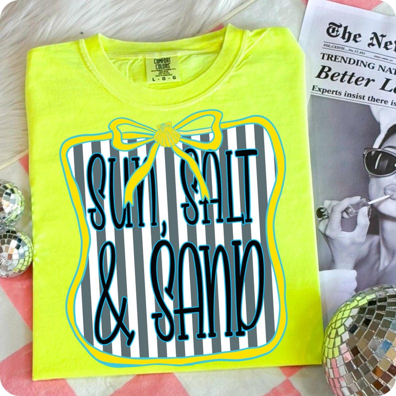 May include: A neon yellow t-shirt with the words "SUN, SALT & SAND" in a decorative design. The design features a bow and a striped background. The shirt is a Comfort Colors brand.