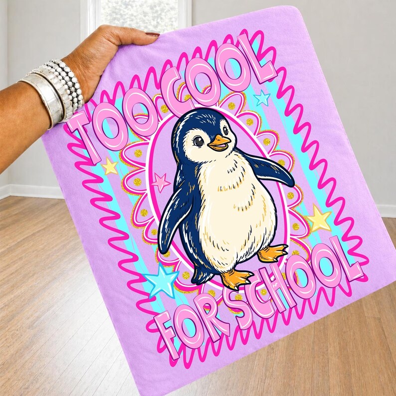 K&ouml;nnte beinhalten: Eine hellviolette Decke mit einem Cartoon-Pinguin und dem Text "TOO COOL FOR SCHOOL" in Pink. Der Pinguin ist blau, wei&szlig; und gelb, umgeben von einem dekorativen Design mit Sternen und Wellenlinien.