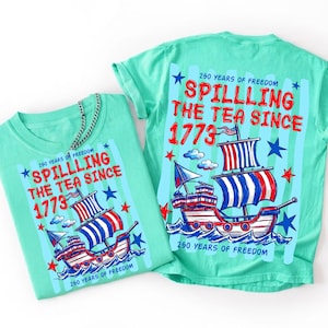 Pu&ograve; includere: Due magliette turchesi con un design patriottico. Il design presenta una nave con vele rosse, bianche e blu, il testo "Spilling the Tea Since 1773" e stelle. Le magliette sono per i 250 anni di libert&agrave;.
