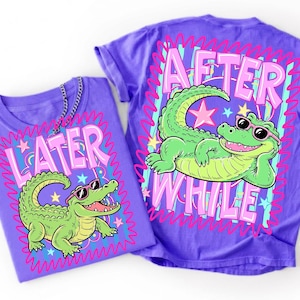 May include: Two purple t-shirts with a cartoon alligator design. One shirt says "LATER" and the other says "AFTER WHILE" in pink bubble letters. The alligator is green and wearing sunglasses.