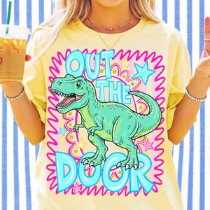 May include: Yellow t-shirt with a turquoise Tyrannosaurus Rex graphic and the words "OUT THE DOOR" in a bubble font. The design includes pink and blue stars and a wavy outline.