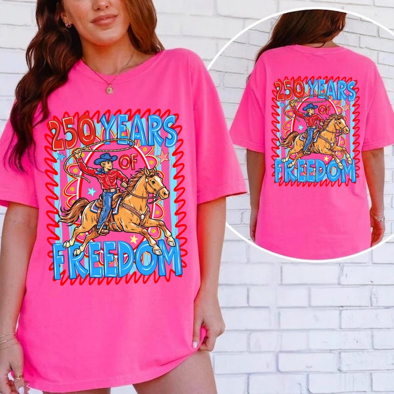 Puede incluir: Camiseta rosa brillante con un gr&aacute;fico de un vaquero montando a caballo, con el texto "250 YEARS OF FREEDOM". El dise&ntilde;o est&aacute; enmarcado por un borde ondulado azul y rojo. La parte trasera de la camiseta tambi&eacute;n tiene el mismo gr&aacute;fico.