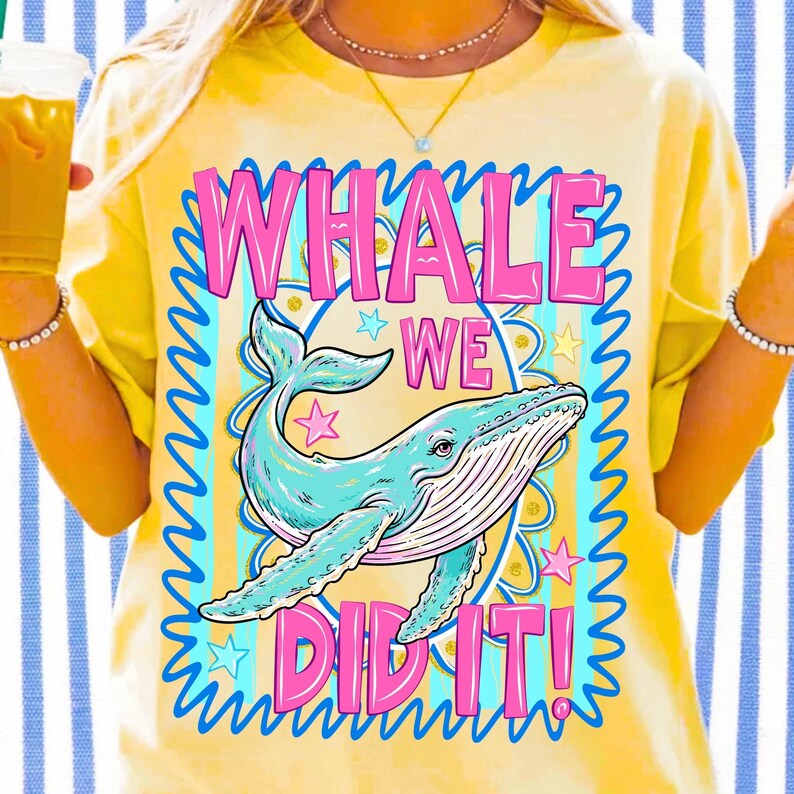 K&ouml;nnte beinhalten: Gelbes T-Shirt mit einer Illustration eines blauen Wals und dem Text "WHALE WE DID IT!" in Pink und Blau. Das Design beinhaltet Sterne und einen dekorativen Rahmen, was einen verspielten Look erzeugt.