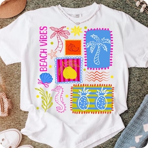 May include: White t-shirt featuring a vibrant "Beach Vibes" design. The graphic includes illustrations of a palm tree, starfish, seashell, seahorse, and pineapples. The design uses a range of colours, including pink, blue, yellow, and orange.