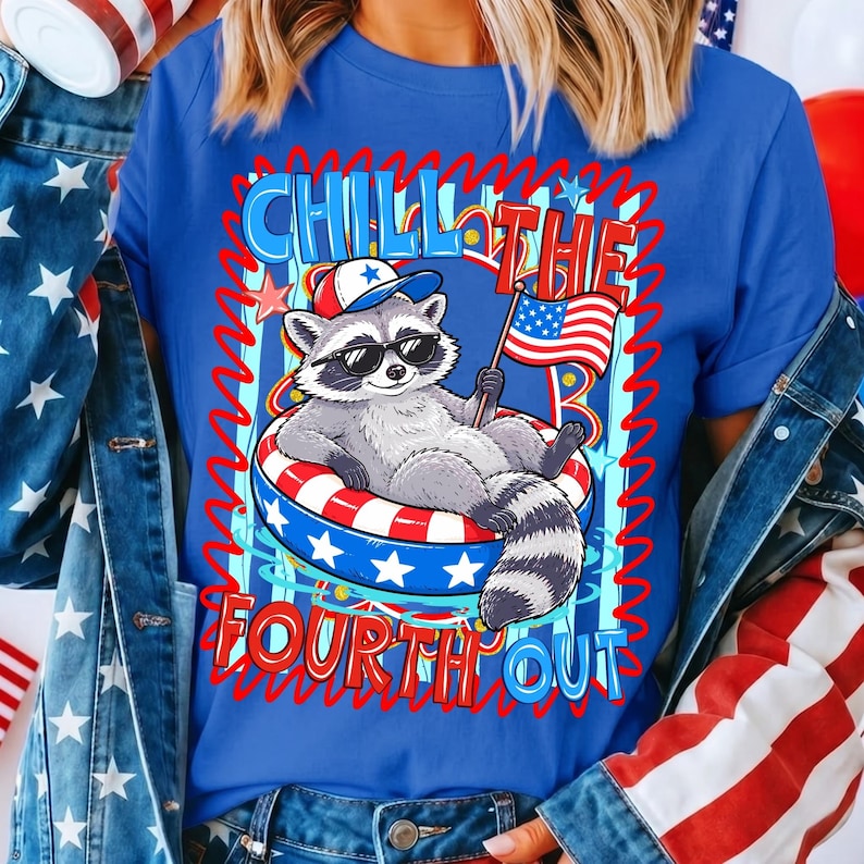 Op de afbeelding: Blauw T-shirt met een cartoon wasbeer met een zonnebril en een patriotische hoed, liggend in een rood, wit en blauw zwemband. Het shirt heeft de tekst "Chill the Fourth Out" in rood en blauw.