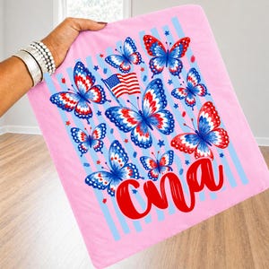 Peut inclure: Un carr&eacute; de tissu rose clair avec une impression graphique de plusieurs papillons aux motifs rouges, blancs et bleus, un petit drapeau am&eacute;ricain et le texte cursif rouge "Cna". Le design inclut des rayures verticales bleu clair et des &eacute;toiles.