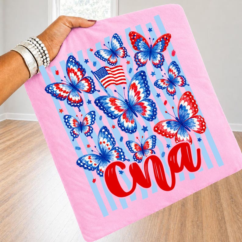 Peut inclure: Un carr&eacute; de tissu rose clair avec une impression graphique de plusieurs papillons aux motifs rouges, blancs et bleus, un petit drapeau am&eacute;ricain et le texte cursif rouge "Cna". Le design inclut des rayures verticales bleu clair et des &eacute;toiles.