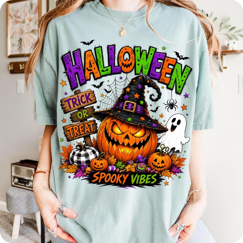 May include: A light green t-shirt featuring a graphic print with the text HALLOWEEN, TRICK OR TREAT, and SPOOKY VIBES. The design includes a large jack-o'-lantern wearing a witch hat, a white ghost, a buffalo plaid pumpkin, and colourful autumn leaves.