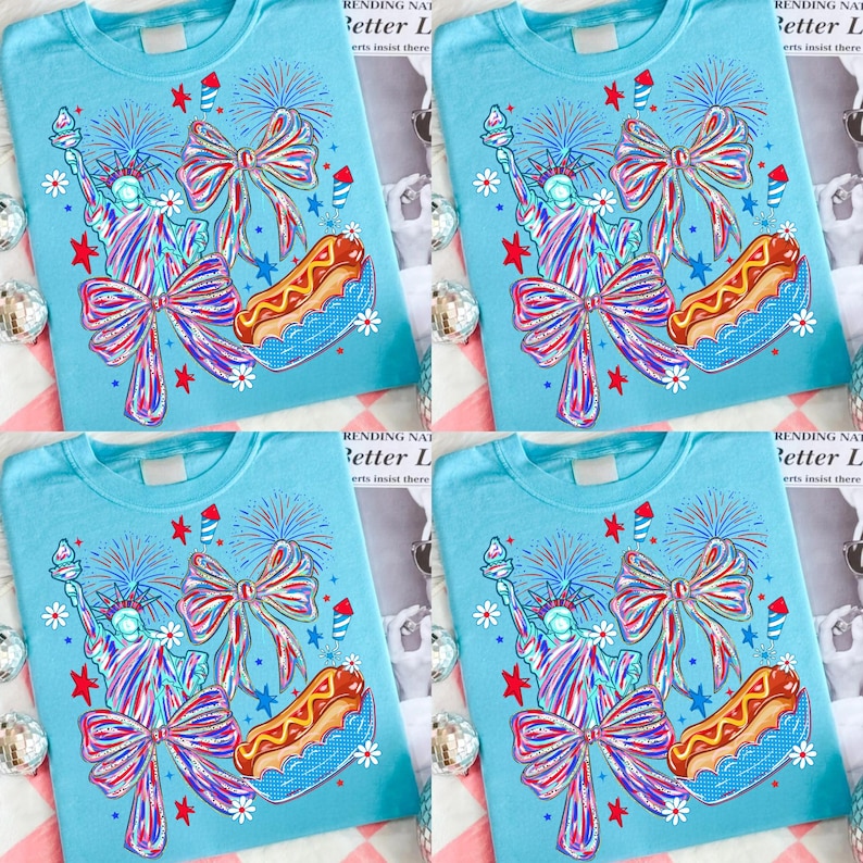 May include: Four light blue t-shirts with a patriotic design. Each shirt features a graphic of the Statue of Liberty, a bow, a hot dog, fireworks, and stars. The text "RENDING NAT Better L erts insist there" is visible.