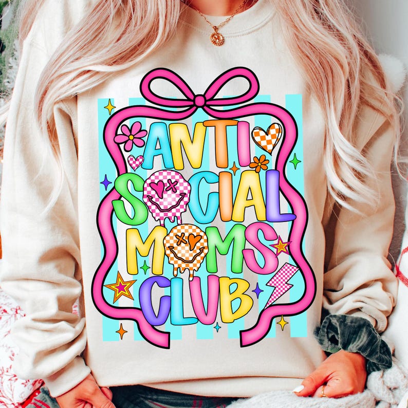 K&ouml;nnte beinhalten: Cremefarbenes Sweatshirt mit einem farbenfrohen Aufdruck "ANTI SOCIAL MOMS CLUB". Das Design zeigt eine rosa Schleife, Blumen, Herzen, Sterne und einen Blitz. Der Text ist in verschiedenen Farben gehalten, darunter Blau, Gelb und Gr&uuml;n.