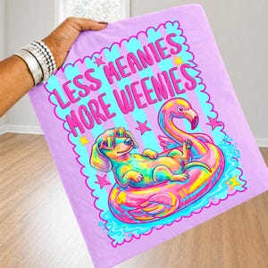 May include: A light purple fabric featuring a graphic print of a colorful dachshund wearing heart-shaped sunglasses, lounging on a pink flamingo pool float. The text reads LESS MEANIES MORE WEENIES in pink letters, surrounded by small stars.