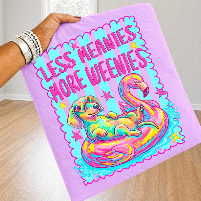 May include: A light purple fabric featuring a graphic print of a colorful dachshund wearing heart-shaped sunglasses, lounging on a pink flamingo pool float. The text reads LESS MEANIES MORE WEENIES in pink letters, surrounded by small stars.