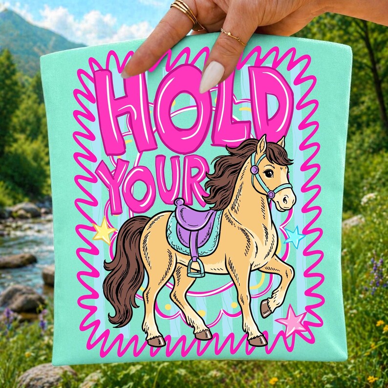May include: A light teal tote bag with the words "HOLD YOUR" in pink bubble letters. A cartoon horse with a purple saddle is featured below the text, with star accents and a pink zig-zag border.