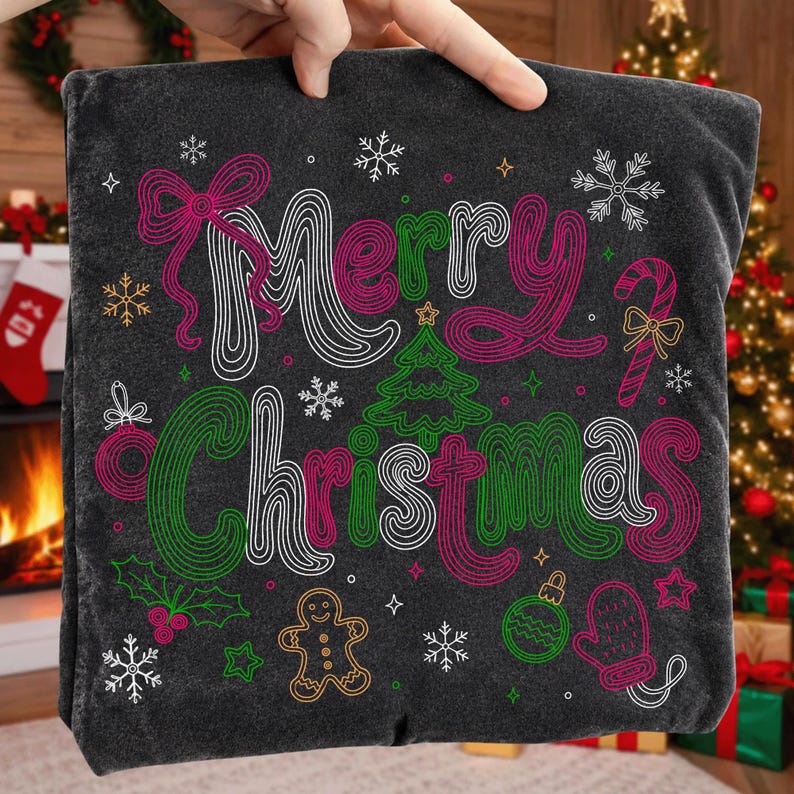 May include: A dark gray t-shirt featuring the text Merry Christmas in a stylized, multi-colored line art font. The design includes festive graphics such as a Christmas tree, a gingerbread man, snowflakes, a candy cane, and a holly sprig.