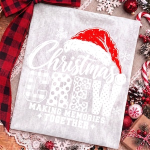 May include: A light gray t-shirt featuring a red Santa hat graphic above the white text "Christmas CREW" and "MAKING MEMORIES TOGETHER". The letters in "CREW" display varied patterns including plaid, polka dots, and leopard print with small snowflakes.