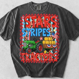 Pode incluir: T-shirt cinza escuro com um gr&aacute;fico "Stars Stripes Tractors" em vermelho e azul. O gr&aacute;fico inclui um trator verde puxando uma carro&ccedil;a de fardos de feno, uma bandeira americana e estrelas.