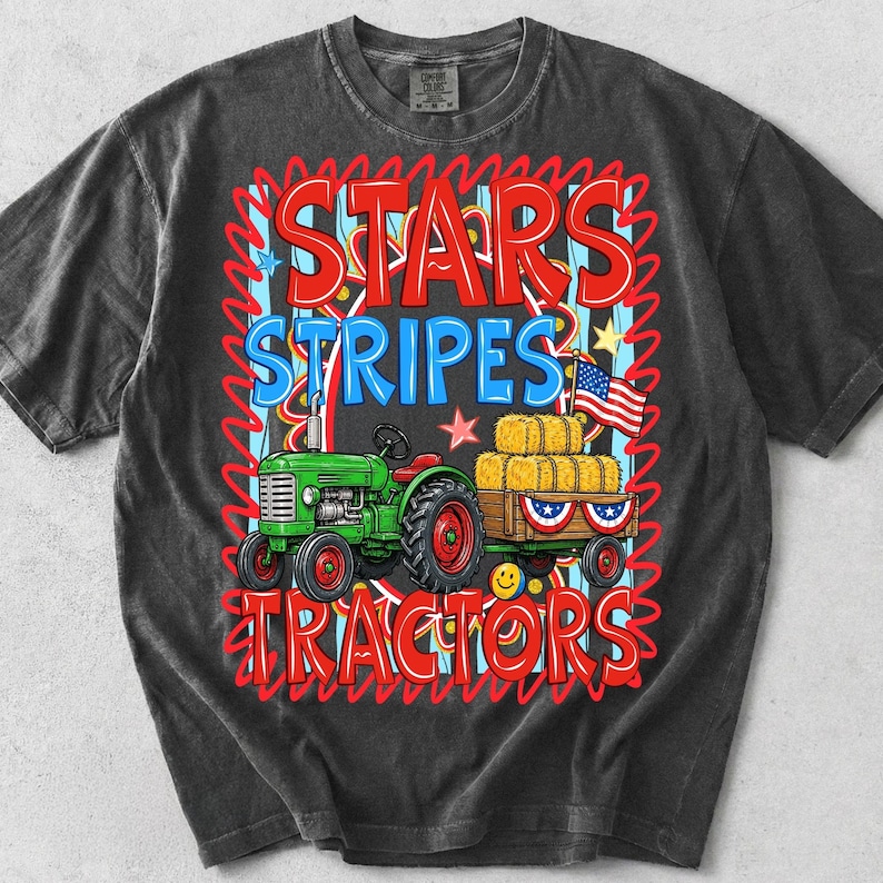 Pode incluir: T-shirt cinza escuro com um gr&aacute;fico "Stars Stripes Tractors" em vermelho e azul. O gr&aacute;fico inclui um trator verde puxando uma carro&ccedil;a de fardos de feno, uma bandeira americana e estrelas.