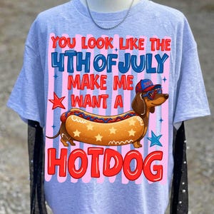 May include: A light gray t-shirt with a graphic featuring a dachshund in sunglasses and a hat, shaped like a hotdog. The text reads "You look like the 4th of July, make me want a hotdog."