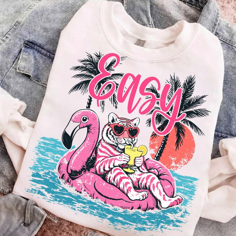 K&ouml;nnte beinhalten: Wei&szlig;es Sweatshirt mit einem Aufdruck eines Tigers mit herzf&ouml;rmiger Sonnenbrille, der auf einem rosa Flamingo-Schwimmer entspannt. Das Wort "Easy" steht in rosa Schrift &uuml;ber dem Tiger. Palmen und ein Sonnenuntergang sind im Hintergrund.